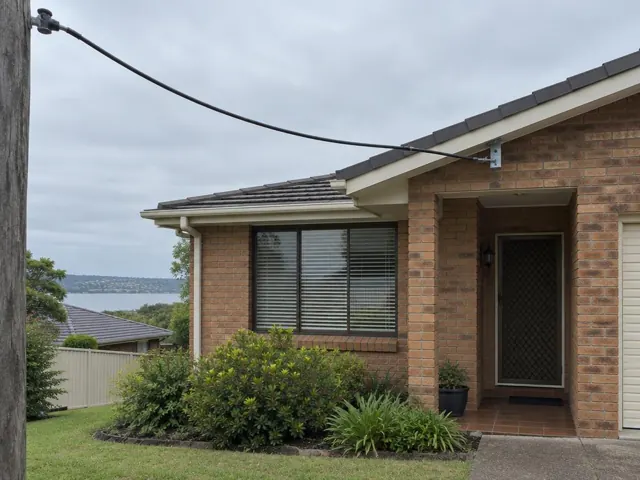 Overhead service cable to a house point-of-attachment bracket on a brick home facade in Eleebana