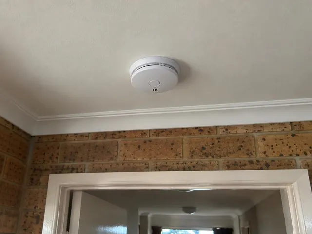 Ceiling smoke alarm above a doorway in a brick interior hallway in Valentine